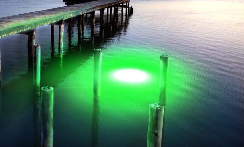 A green colored underwater LED light near a dock.
