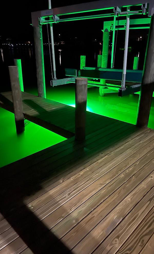 A green underwater LED light next to a wooden dock. 